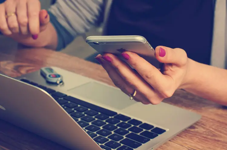 mains d'une femme regarde son smartphone devant un ordinateur