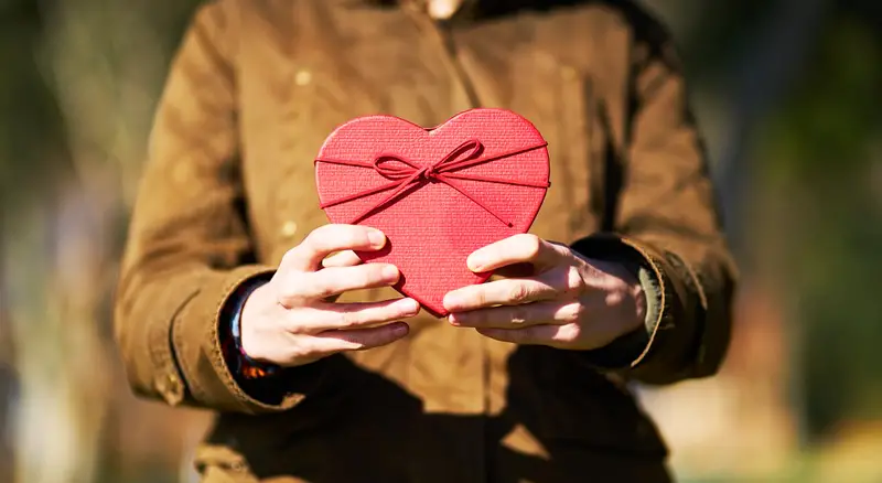 les mains d'une personne qui offre un cadeau en forme de coeur