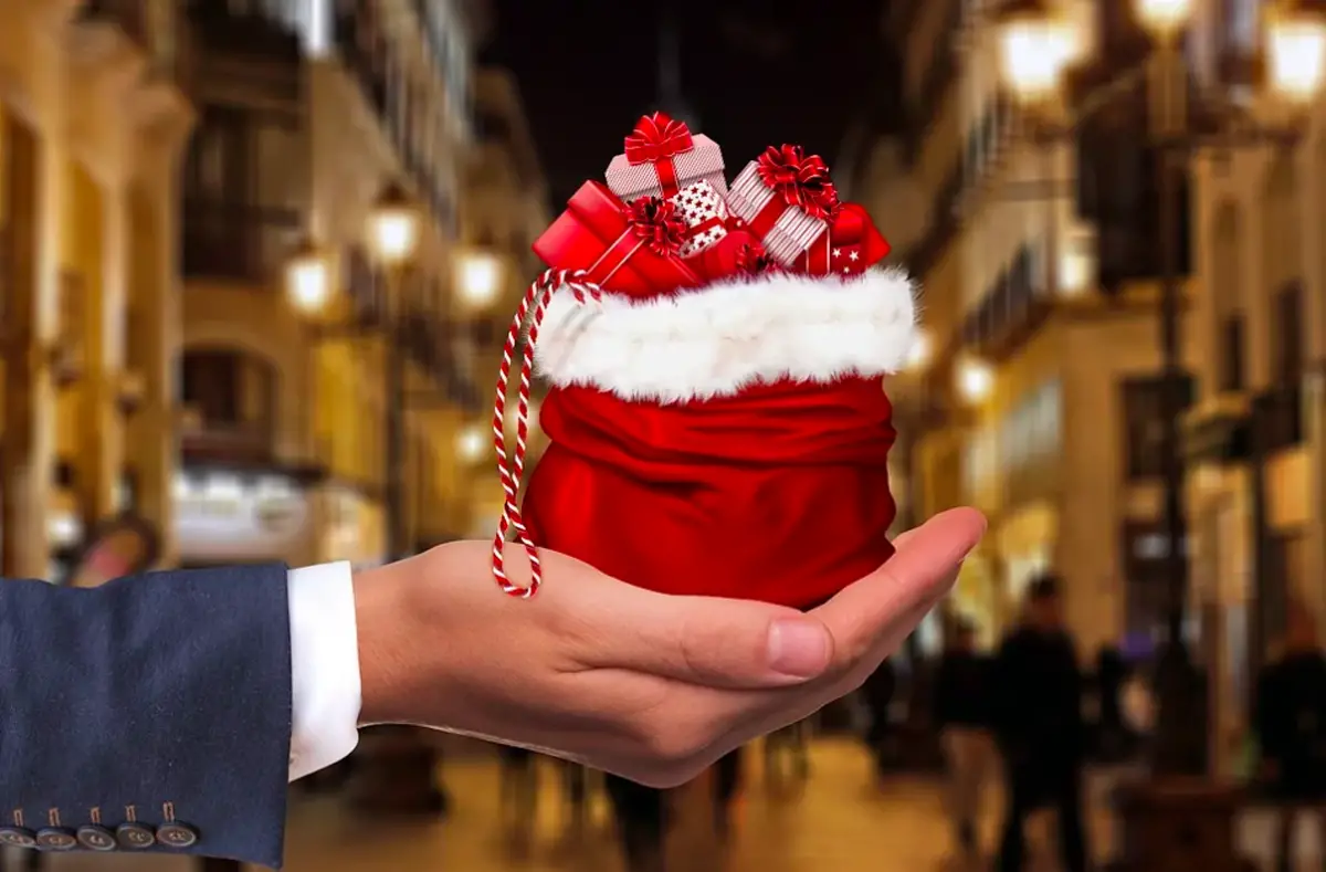 bras d'un homme en costume tend un petit cadeau de noel dans le creux de sa main