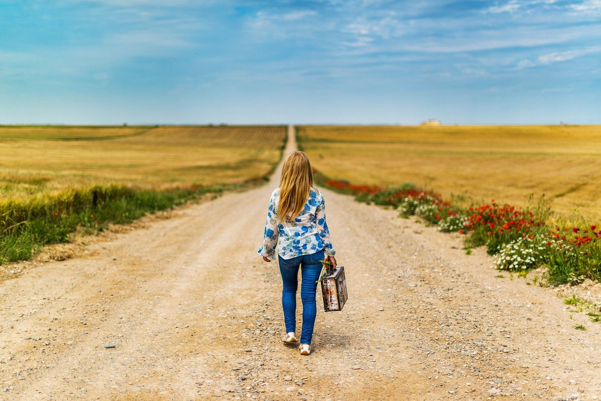 femme seule marche au milieu d'une route avec sa valise